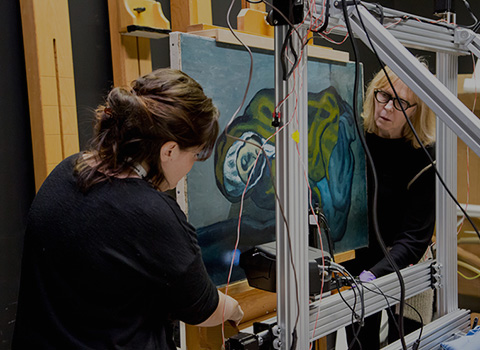 Two researchers set up a scanning apparatus to analyze a painting